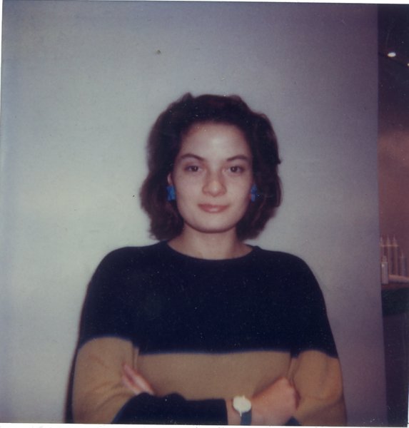 Femme bras croisés à pull bicolore marron et noir et clips d’oreille bleus.