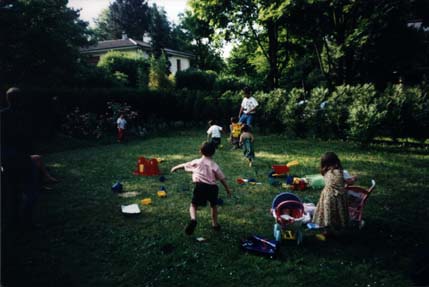 Un homme et des enfants dans un jardin avec jouets éparpillés dans l’herbe.