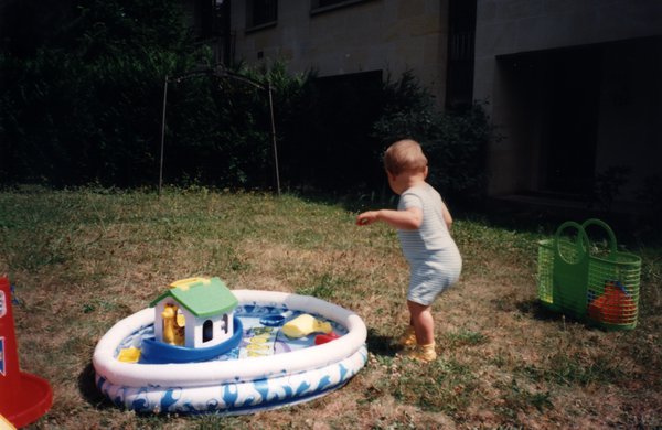 Enfant debout dans un jardin avec jouets et mini-piscine gonflable.