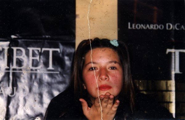 Jeune femme de face avec cheveux noirs et barrette bleue avec une affiche en arrière-plan. Image avec déchirure, reconstituée.