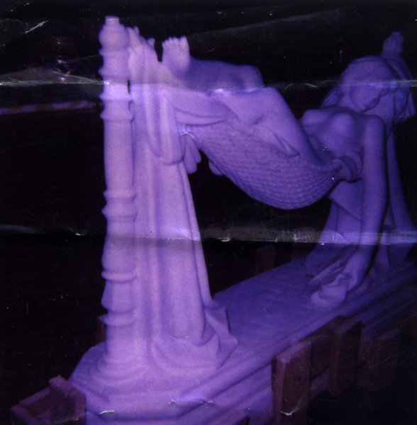 Statue en stuc de femme allongée seins nus dans un hamac accroché à deux pilastres. Image avec froissure et pliure.