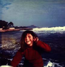 Jeune fille à pull rouge riant devant les vagues.