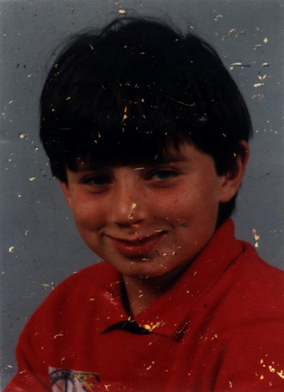 Petit garçon brun souriant en polo orange. Image abîmée.