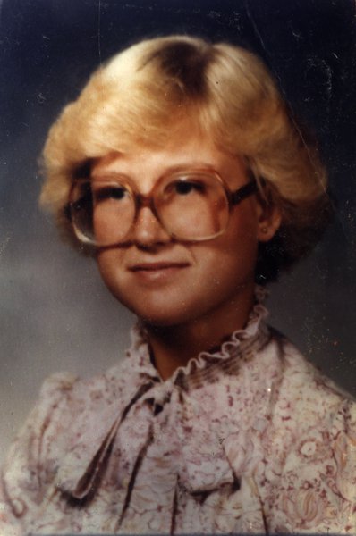 Femme blonde avec grandes lunettes de vue et chemise à col Claudine.
