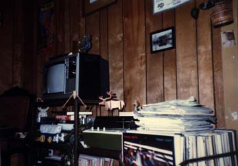Meuble à étagères avec téléviseur, tourne disque, et pile de disques 33 tours plaçés contre un mur lambrissé.