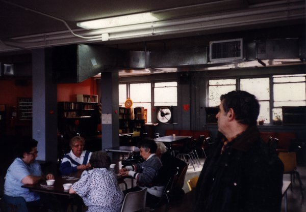 Femmes âgées assises à une table devant des tasses blanches dans une salle de café, homme en avant-plan.