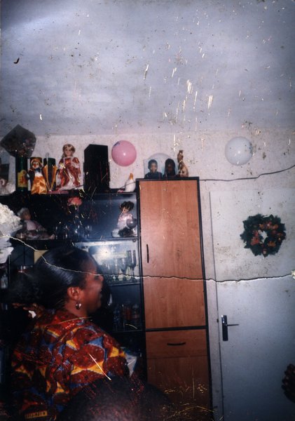 Femme de profil devant un meuble à étagères et une porte avec décoration.