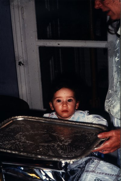 Petit enfant assis face à un plateau en argent tenu par une femme de profil.