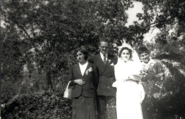Mariée en blanc au bras d’un marié en costume noir accompagnés d’un jeune garçon et d’une jeune fille. Image abîmée. Noir et blanc