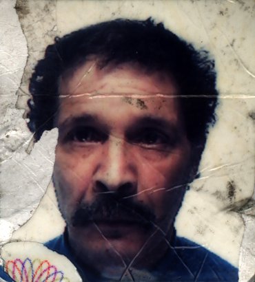Visage d’homme brun avec moustache et cheveux frisés. Image avec salissures.