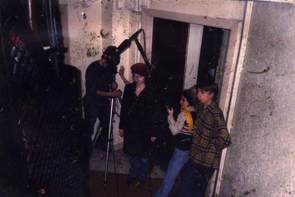 Groupe de personnes avec caméra sur trépied devant une porte, de nuit.ᴬᴵ