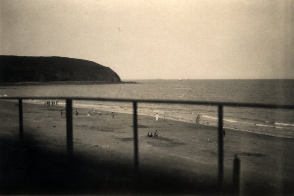 Vue d'une plage à travers une balustrade, falaise en arrière-plan. Noir et blanc.ᴬᴵ