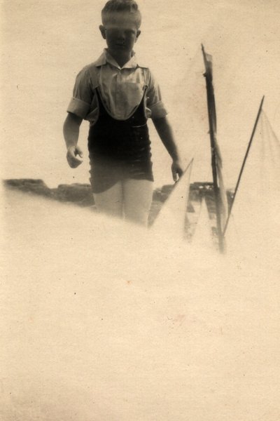 Garçon debout sur une plage près de voiliers. Image surexposée. Noir et blanc.ᴬᴵ