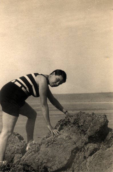 Femme en maillot de bain rayé penchée sur des rochers. Noir et blanc.ᴬᴵ