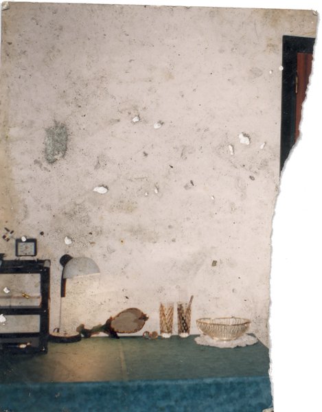 Console avec lampe et verres devant un mur blanc. Image très abîmée.