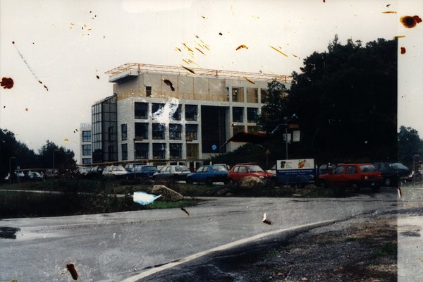 Bâtiment en construction avec voitures garées au premier plan. Image tachetée.ᴬᴵ