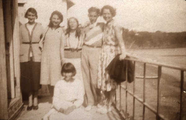 Groupe de femmes et une fillette posant sur une terrasse au bord de mer. Noir et blanc.ᴬᴵ