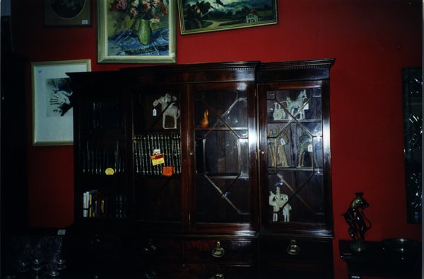 Bibliothèque à vitrine devant un mur rouge où sont accrochés des tableaux.