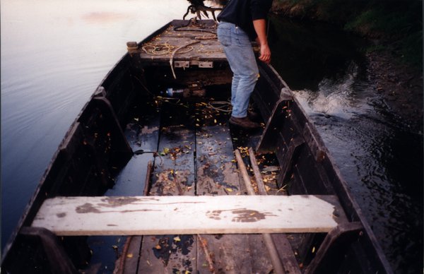 Homme en jean debout dans une barque sur l’eau.