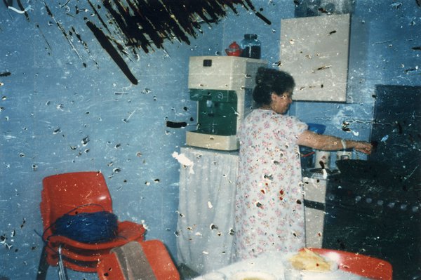 Femme brune en robe à fleurs dans sa cuisine. Image abîmée.