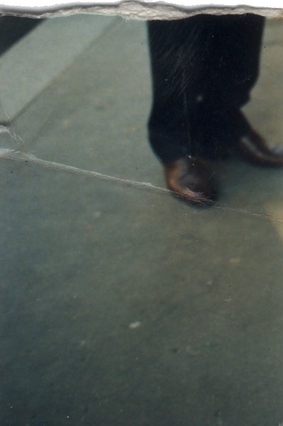 Jambes recouvertes d’un pantalon et chaussures. Fragment déchiré.