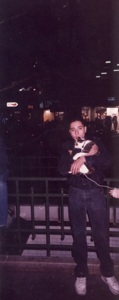 Homme la nuit devant la balustrade d’un métro parisien avec un chat dans les bras.