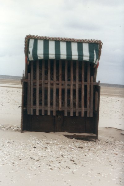 Cabine de bain en bois sur une plage avec ciel nuageux.