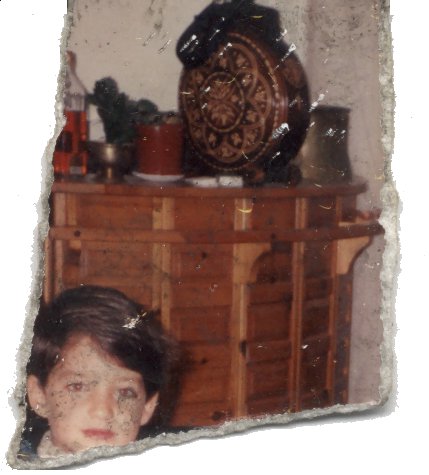 Visage d’enfant brun devant une commode. Fragment déchiré.