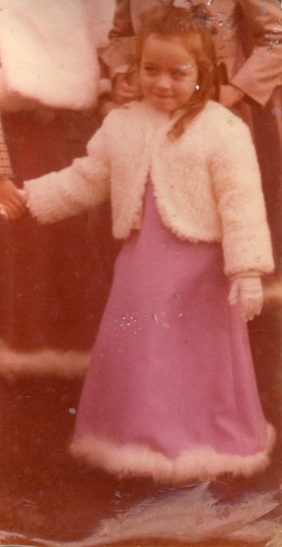 Petite fille blonde en robe longue et gants blancs.