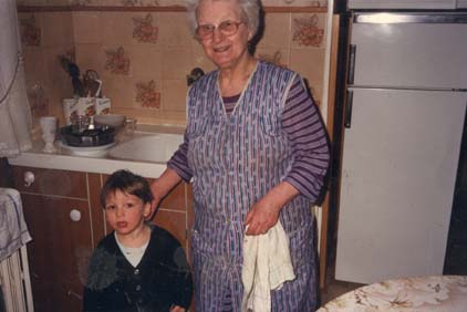 Femme âgée en blouse bleue et petit garçon dans une cuisine.