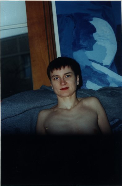 Femme brune, le buste nu, assise devant une peinture abstraite bleue.
