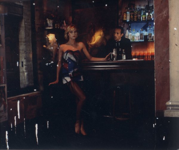 Femme blonde en bustier et mini jupe devant un bar avec barman.