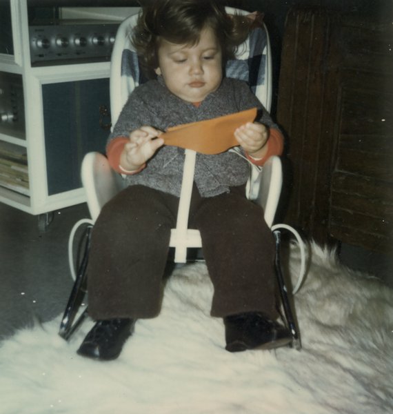 Petit enfant dans un siège bébé posé sur un tapis à grands poils blancs.
