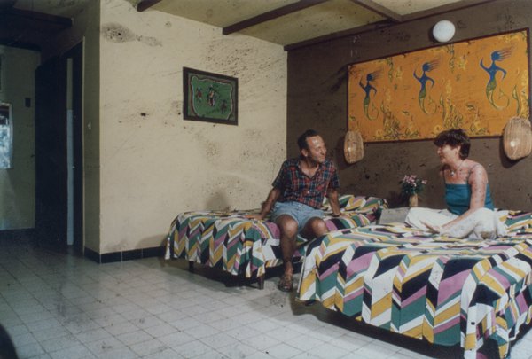 Un homme et une femme assis sur des lits jumeaux recouverts de couvertures bariolées.