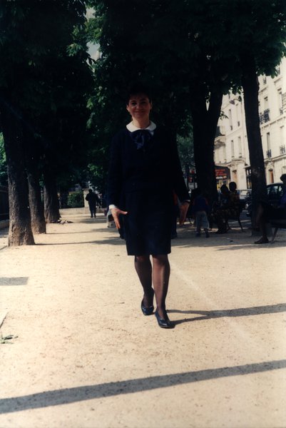 Femme en tailleur sombre marchant sur une allée bordée d'arbres.ᴬᴵ