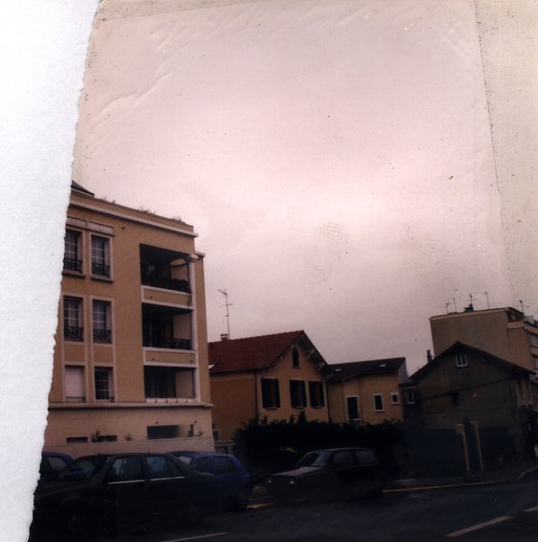 Immeubles, rue, et ciel voilé.