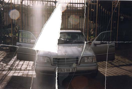 Mercedes blanche toutes portes ouvertes devant la grille d’un parc, en arrière-plan belle demeure. Image déchirée en partie reconstituée.