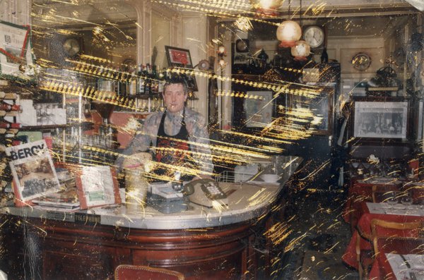Homme en tablier debout derrière un comptoir de bistrot. Image avec rayures.