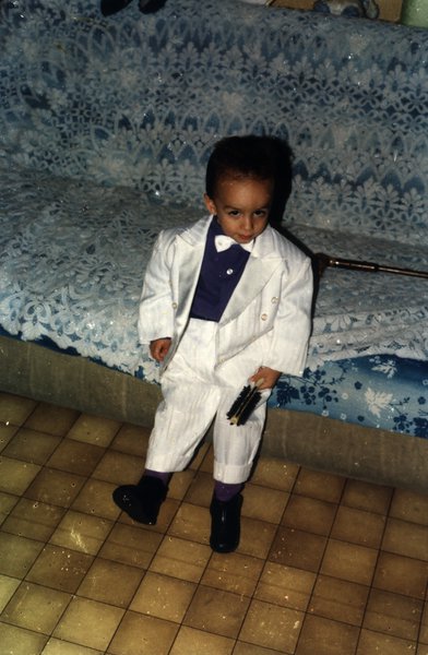 Enfant en costume blanc devant un canapé recouvert de dentelle.ᴬᴵ
