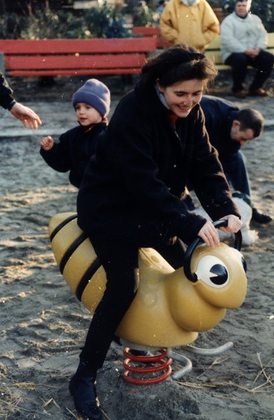 Femme et enfants sur un jeu à ressort en forme d'abeille dans un parc.ᴬᴵ