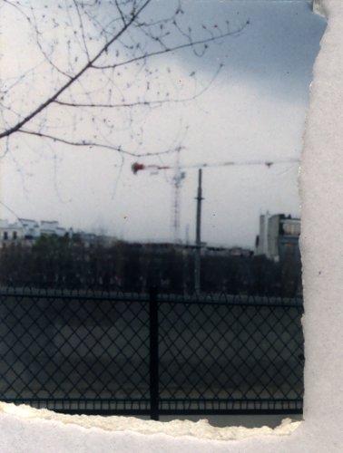 Vue d'une ville avec une grue à travers une clôture. Fragment déchiré.ᴬᴵ