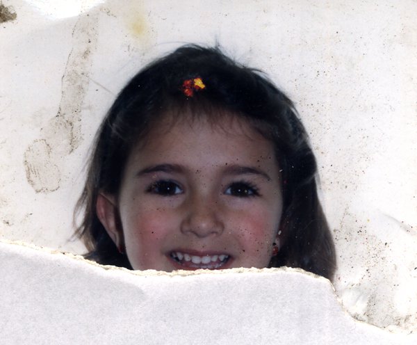 Visage souriant d'une fillette aux cheveux ornés d'une barrette fleurie. Fragment déchiré.ᴬᴵ