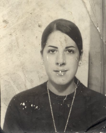 Visage de jeune femme aux cheveux bruns tirés et corsage sombre. Image avec pliure. Noir et blanc.