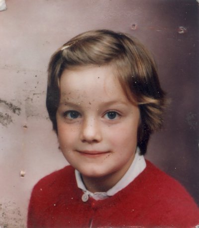 Visage de petite fille à cheveux courts blond, barrette et pull rouge.