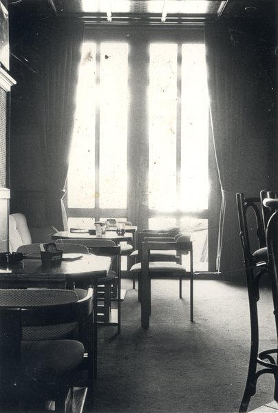 Tables et chaises dans une salle de restauration, grande fenêtre en arrière-plan. Noir et blanc.