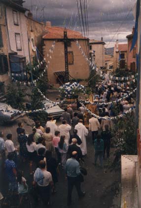 Procession religieuse dans un village décoré de guirlandes.