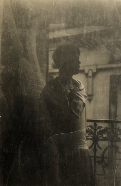 Silhouette d'une femme sur un balcon à balustrade en fer forgé. Noir et blanc.ᴬᴵ