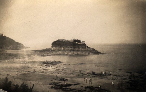 Vue surélevée d'un îlot fortifié et d'une plage avec des baigneurs. Noir et blanc.ᴬᴵ