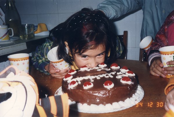 Petite fille brune le menton enfoui dans un gâteau au chocolat posé sur une table. Image avec date et heure en impression.
