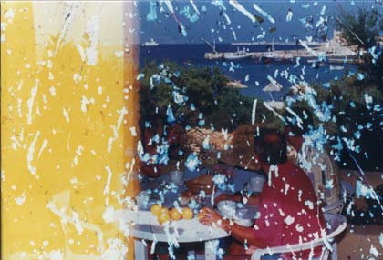 Hommes et femmes autour d’une table où sont posés des oranges devant un panorama côtier avec port et bateaux. Image très abîmée.